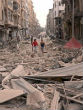 Image of Two people walk through what is left of a Syrian neighborhood.