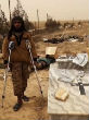 Image of ISIS militant stands with the help of crutches beside destroyed Christian headstone.