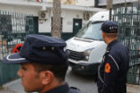 Image of Moroccan security forces stand guard as a van leaves the court