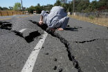 Image of A road worker examines damage done by a quake in California. 